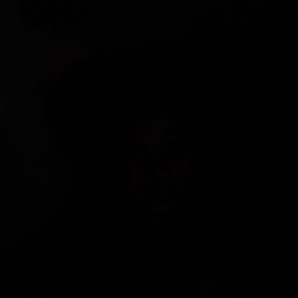 A dark, low-key photograph of a test setup in a lab, with deep shadow and muted metallic tones.