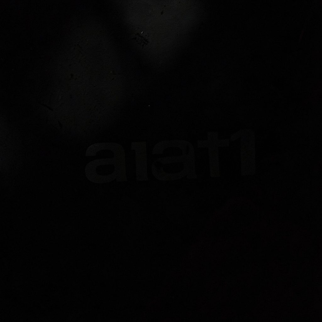 A shadow-rich image of a sponsor logo plaque, with muted blush and slate accents against a dark background.